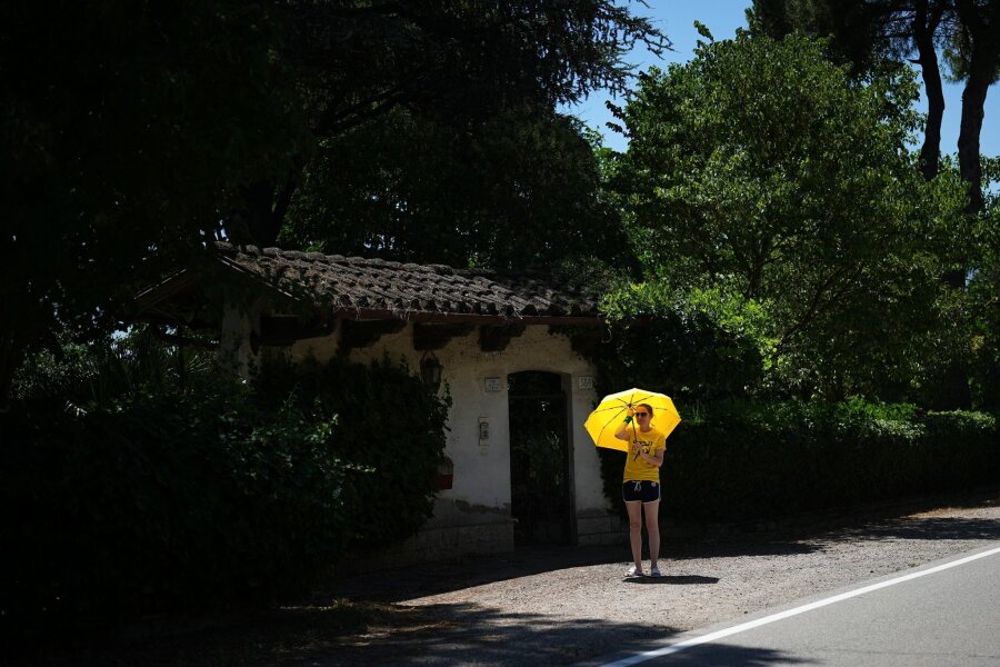 Bilder des Tages vom 30.06.2024 - Schwitzen am Wegesrand: Unter einem Schirm wartet eine Zuschauerin auf die Teilnehmer der Tour de France in Italien. Bei Temperaturen bis zu 36 Grad legen die Radfahrer die Strecke von Cesenatico bis Bologna zurück.