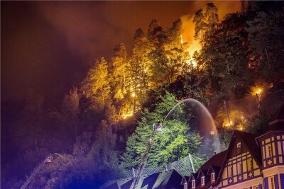 Brände im Elbsandsteingebirge - ganze Waldgebiete gesperrt - Flammen lodern direkt hinter Häusern im böhmischen Hrensko, während ein Feuerwehrmann zu löschen versucht. 
