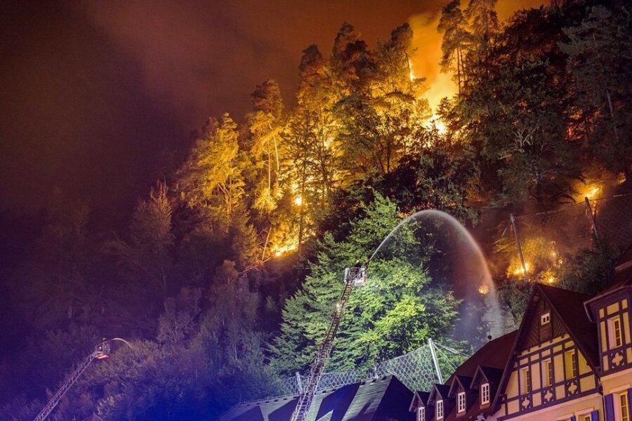 Flammen lodern direkt hinter Häusern im böhmischen Hrensko, während ein Feuerwehrmann zu löschen versucht. 