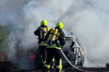 Brennendes Auto löst Feldbrand aus - Die Kameraden beim Löschen des Fahrzeugs und Feldbrandes.
