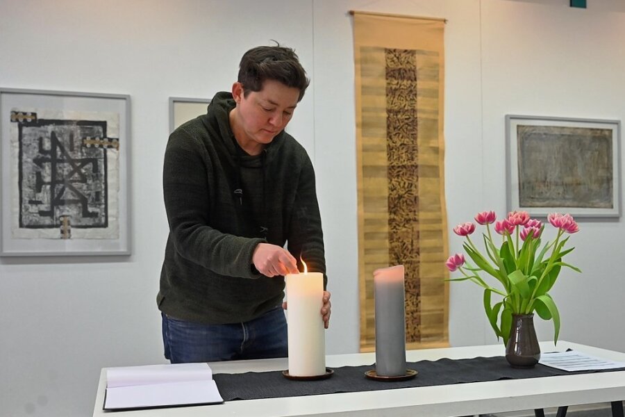 Daniela Schleich, Mitarbeiterin beim Chemnitzer Künstlerbund, entzündet in der Ausstellung, die verstorbenen Künstlern gewidmet ist, eine Kerze. Im Hintergrund sind Arbeiten von Fritz Schönfelder zu sehen. 