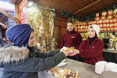 Churros auf dem Zwickauer Weihnachtsmarkt schmecken nach Liebe - Hmmm, lecker: Esraa Alferekh (rechts) reicht Rayan Bitar am Stand von Ahmad Kiwan (Mitte) eine Portion frisch gebackene Churros. 