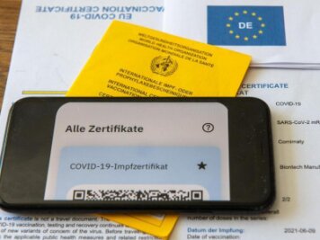 Corona-Lage in Chemnitz: Startprobleme bei digitalem Impfpass -             Ein Impfpass und ein Smartphone, auf dem die App CovPass läuft.