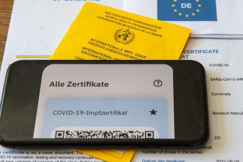 Corona-Lage in Chemnitz: Startprobleme bei digitalem Impfpass -             Ein Impfpass und ein Smartphone, auf dem die App CovPass läuft.