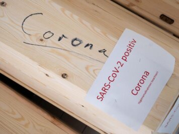            Särge mit Aufschrift "Corona" und "SARS-CoV-2 positiv - Corona" stehen in einer Kühlkammer.