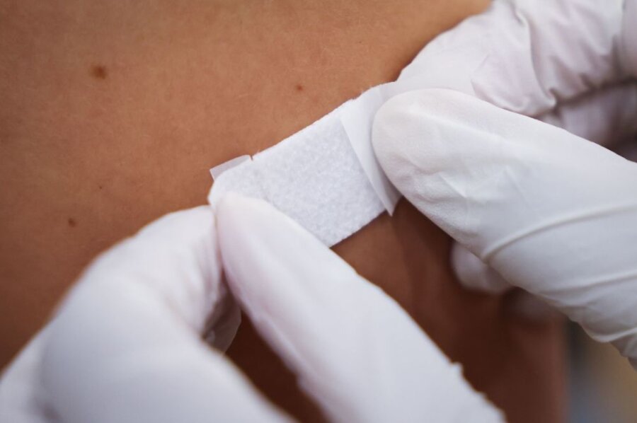 Eine Ärztin klebt einem Mann nach der Impfung ein Pflaster auf den Arm.