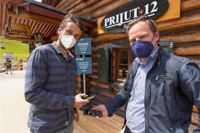 Covid-Ex-Modell in Oberwiesenthal: Die ersten Gäste werden erwartet - Philipp Heinrich, Inhaber des Restaurants "Prijut 12", und Covid-Exit-Projektmanager Erik Schulze (v. l.) demonstrieren, dass im einfachsten Fall ein Smartphone genügt, um sich registrieren zu lassen. 