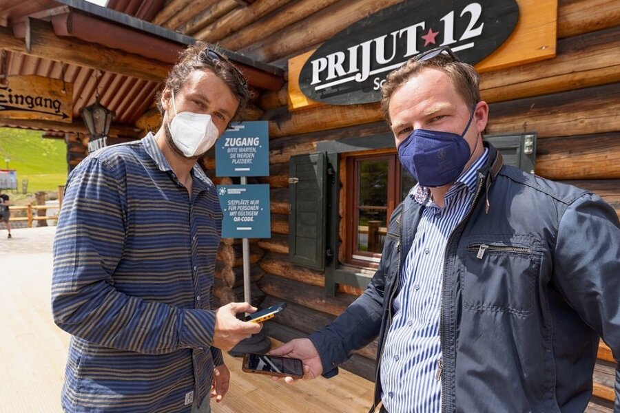 Philipp Heinrich, Inhaber des Restaurants "Prijut 12", und Covid-Exit-Projektmanager Erik Schulze (v. l.) demonstrieren, dass im einfachsten Fall ein Smartphone genügt, um sich registrieren zu lassen. 