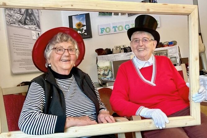 Damen im Rahmen haben viel Spaß - Irene Keller (l.) und Gerda Haase posieren mit Freude im Bilderrahmen. Das Fotoshooting mit Hüten war Teil der Mottowoche in der Erlabrunner Tagespflege. 