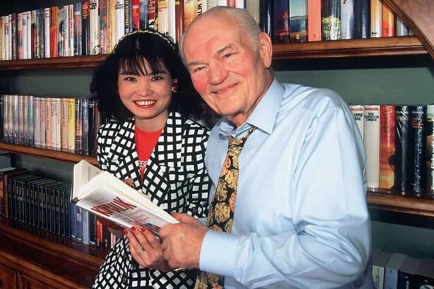 Heinz G. Konsalik und seine Lebensgefährtin Ke Gao posieren am 10.04.1996 in Salzburg (Österreich) vor einem Regal, in dem alle Bücher des Erfolgsautors aufbewahrt werden.