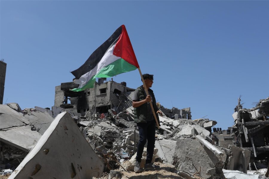Deutschland in der Zwickmühle - Ein Palästinenser hält in Chan Junis die palästinensische Fahne in der Hand, während er auf Trümmern durch israelischen Beschuss steht. Norwegen, Irland und Spanien werden Palästina demnächst als Staat anerkennen.