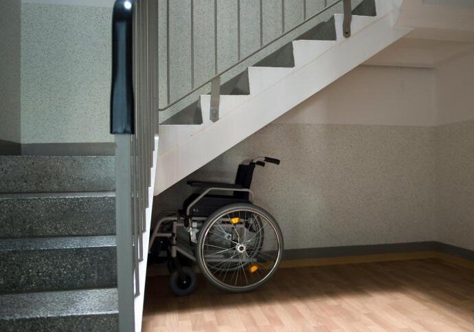 Ein Rollstuhl steht unter einer Treppe in einem Wohnhaus in Sachsen.