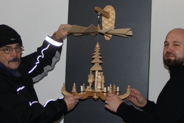 Peter Laube (links) und Christian Landrock platzieren eine traditionelle Hängepyramide mit drei Figuren und einem geschnitzten Baum als Achse in der Mitte in der Ausstellung. 