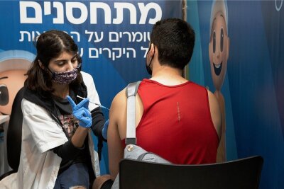 Dritte Impfung - ja oder nein? - In Israel sind die Booster-Impfungen gegen Corona in vollem Gang - auch für Jüngere. Eine medizinische Angestellte in Jerusalem verabreicht einem Mann eine dritte Dosis. 