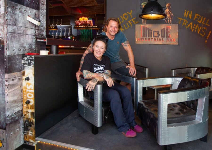 Duo öffnet Bar in Industriedesign - Caroline Pflug und Michael Baumgärtel in ihrer neuen Bar Unique. Links im Hintergrund sieht man den grünlich leuchtenden Wasserfall über der Theke. 