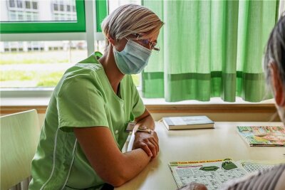 Ehrenamt im Krankenhaus Mittweida: Der Besuch der Grünen Dame - Die Grüne Dame Stefanie Jahr lässt sich im Krankenzimmer von Patientin Renate Baum ein Rätselheft erklären. 