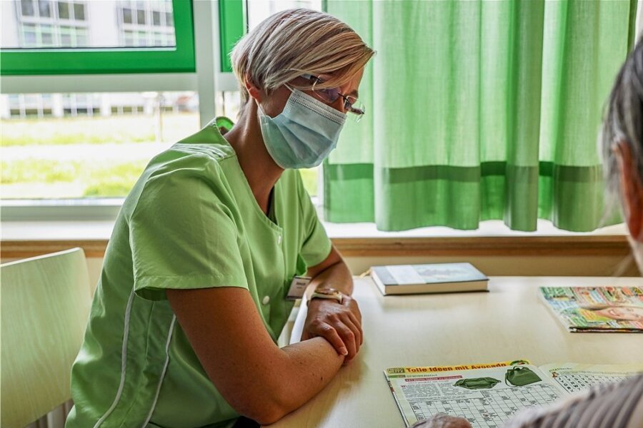 Ehrenamt im Krankenhaus Mittweida: Der Besuch der Grünen Dame - Die Grüne Dame Stefanie Jahr lässt sich im Krankenzimmer von Patientin Renate Baum ein Rätselheft erklären. 
