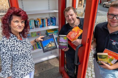 Eicher Telefonhäuschen kehrt nach Odyssee in die Heimat zurück - Auf dem Treuener Markt steht jetzt eine Büchertauschzelle. Bürgermeisterin Andrea Jedzig, ließ sich von den Kulturbanausen Maik Strauß und Lukas Lorber (rechts) zeigen, welche Bücher man dort finden kann. 