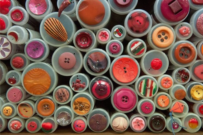 Ein Blick durchs Knopfloch - Bei Knöpfen lässt sich aus dem Vollen schöpfen: keine Form, keine Farbe, die es nicht unter ihnen gibt. Hier liegen sie in einem Laden für Nähbedarf, nach roten Farbtönen sortiert, zur Ansicht auf den Knopfdosen. 
