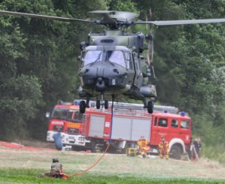 Einsatzkräfte in Alarmbereitschaft - Auch die Bundeswehr unterstützt mit ihren Kräften die Brandbekämpfung im Naturpark - hier im Foto ein Hubschrauber, der mit einem Löschwasser-Außenlastbehälter am Ufer der Elbe abhebt. 