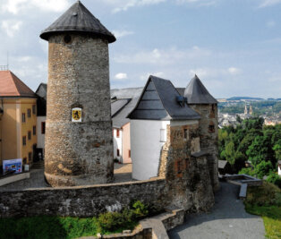 Entdeckungsreise auf Schloss Voigtsberg - Als der Bergfried noch Rückzugsort bei Raubüberfällen war, soll sich der Eingang in Höhe des Wappens befunden haben, die ursprüngliche Höhe der Burgmauer ist am weißen Gebäude rechts erkennbar.