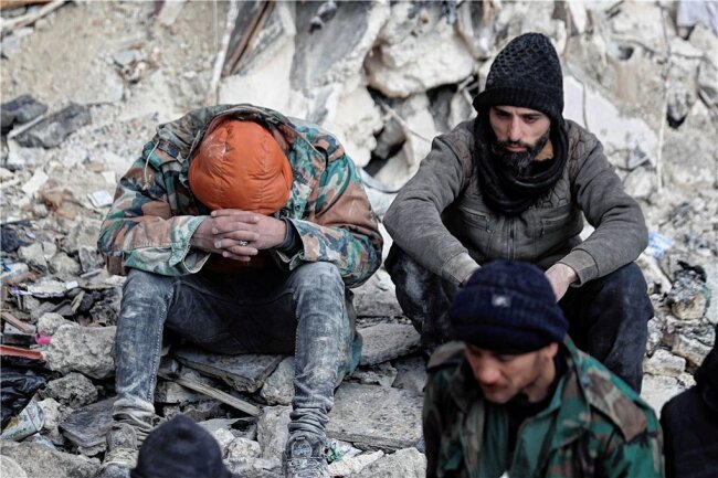 Erdbebenkatastrophe in der Türkei: Stimmen unter den Trümmern - Erschöpfung und Verzweiflung: Zwei Männer sitzen auf den Trümmern eingestürzter Gebäude in der syrischen Stadt Aleppo. 