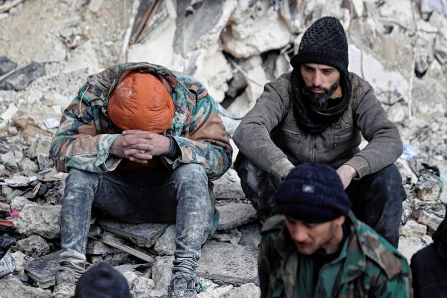 Erdbebenkatastrophe in der Türkei: Stimmen unter den Trümmern - Erschöpfung und Verzweiflung: Zwei Männer sitzen auf den Trümmern eingestürzter Gebäude in der syrischen Stadt Aleppo. 