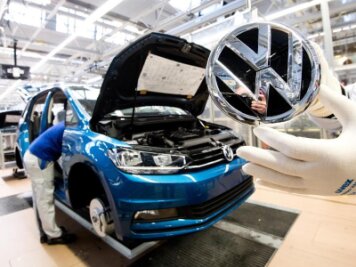 Erfolgsprämie für VW-Mitarbeiter steigt auf 4750 Euro - Ein Mitarbeiter zeigt ein VW Logo kurz vor Einbau in einen Volkswagen Touran.