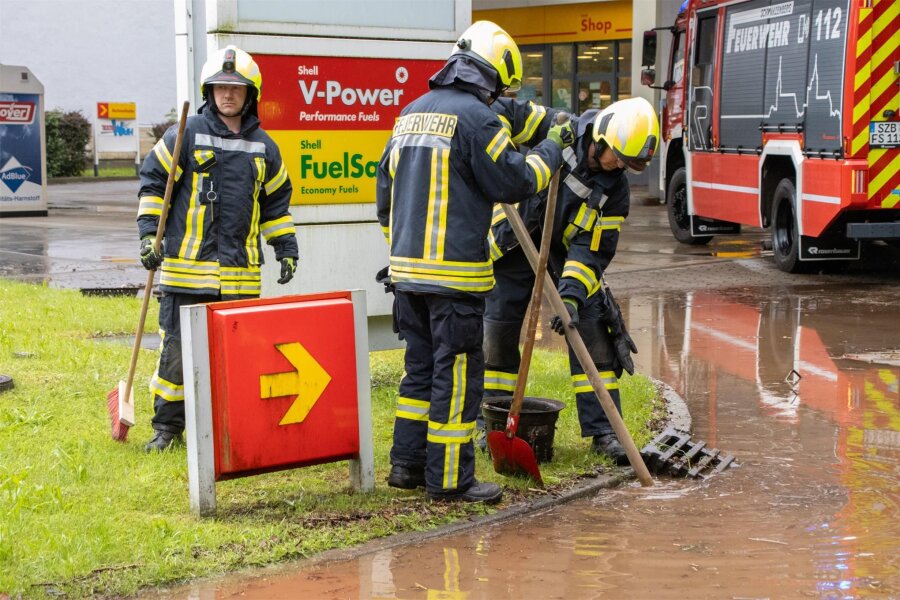 Erste Gewitter und Starkregen kommen im Erzgebirge an - Kameraden der Feuerwehr säubern an einer Tankstelle in Schwarzenberg Gullys, damit das Wasser ablaufen kann.