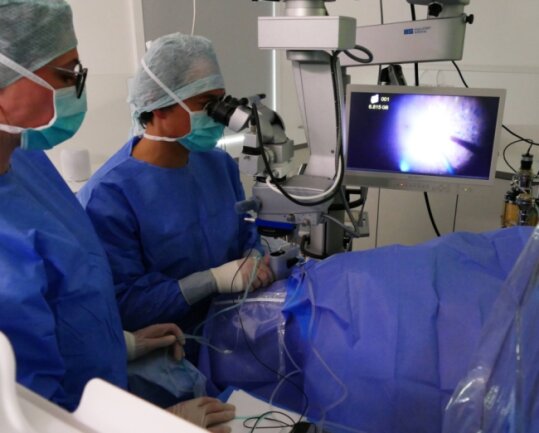Assistiert von Jasmin Schmidt, führt Prof. Dr. Kai Januschowski eine der ersten ambulanten Netzhautoperationen im Zschopauer Augenzentrum durch. Der Bildschirm zeigt den Eingriff vergrößert. 