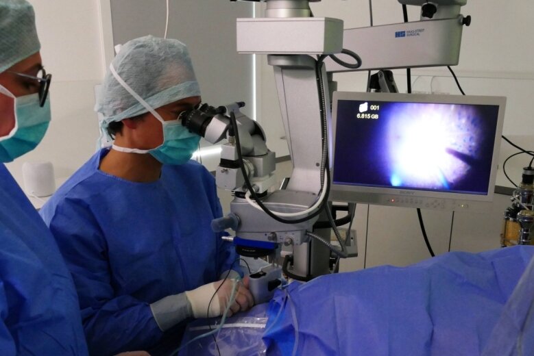 Assistiert von Jasmin Schmidt, führt Prof. Dr. Kai Januschowski eine der ersten ambulanten Netzhautoperationen im Zschopauer Augenzentrum durch. Der Bildschirm zeigt den Eingriff vergrößert. 