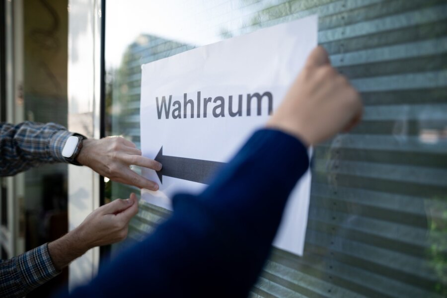 Europawahl in Deutschland angelaufen - Wahlhelfer hängen einen Zettel, auf dem „Wahlraum“ steht, auf.