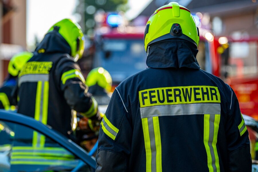 Feuer im Flur - Mehrfamilienhaus in Görlitz evakuiert - Feuerwehrleute stehen um ein Auto, das einen Unfall gehabt hat.