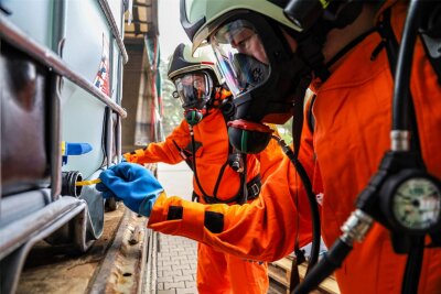 Feuerwehren in Lößnitz alarmiert: Gefahrgutzug rückt zur Landtechnik an - Die Einsatzkräfte testen in Schutzanzügen den Inhalt des etwa 1000 Liter fassenden Gefahrstoffbehälters, der zum Übungszweck mit Wasser gefüllt ist.