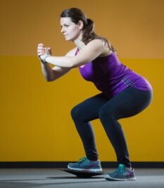Fit mit Functional Training - Beinmuskeln: Für die Squats auf dem Balance- board Beine hüftbreit nebeneinander, das Gesäß weit nach hinten, Rücken gerade Arme nach vorn, hoch und runter.