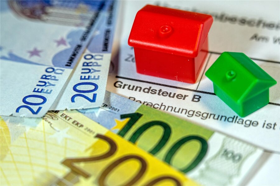 Frankenberg: Daten von 2018 als Basis für neue Grundsteuer - Spielzeughäuser und die Nachbildung von Euro-Geldscheinen liegen auf einem Bescheid für die Entrichtung der Grundsteuer. Für die Abgabe gilt ab 2025 eine Reform.