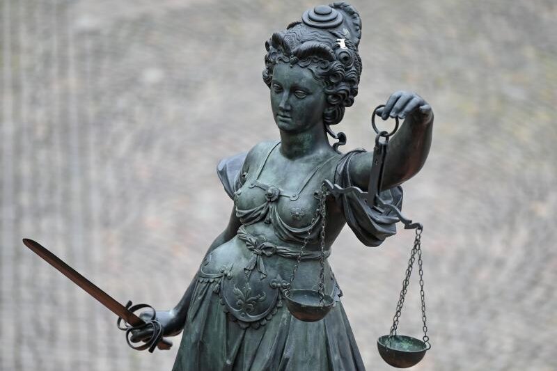            Eine Statue der Justitia hält eine Waage und ein Schwert in der Hand.