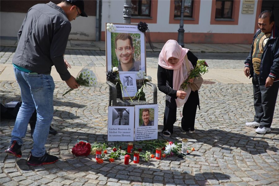 Gedenken an den in Mannheim getöteten Polizisten: In Zwickau setzen Afghanen ein Zeichen gegen Extremismus - Bei der Kundgebung für Demokratie auf dem Kornmarkt legten Menschen als Zeichen von Mitgefühl und Trauer Blumen vor ein Foto des getöteten Polizisten Rouven Laur.