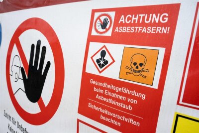 Gewerkschaft warnt vor "Asbest-Falle": Bis zu 182.000 Häuser in Sachsen betroffen - Ein Schild mit der Aufschrift "Achtung Asbestfasern" hängt an einem Bauzaun. Die Industriegewerkschaft Bauen-Agrar-Umwelt (IG BAU)warnt vor einer neuen Asbest-Gefahr. 