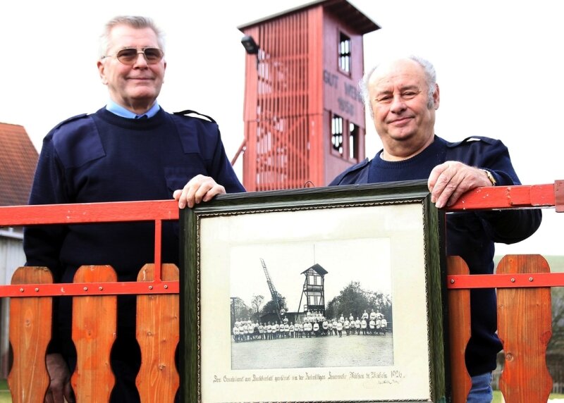 Halbes Jahrhundert bei der Wehr - <p class="artikelinhalt">Joachim Steinert (rechts) und Bernd Zenner mit einem historischen Foto von 1912 vor dem Steigerturm der Michelner Wehr, der auch heute noch an dieser Stelle steht.</p>