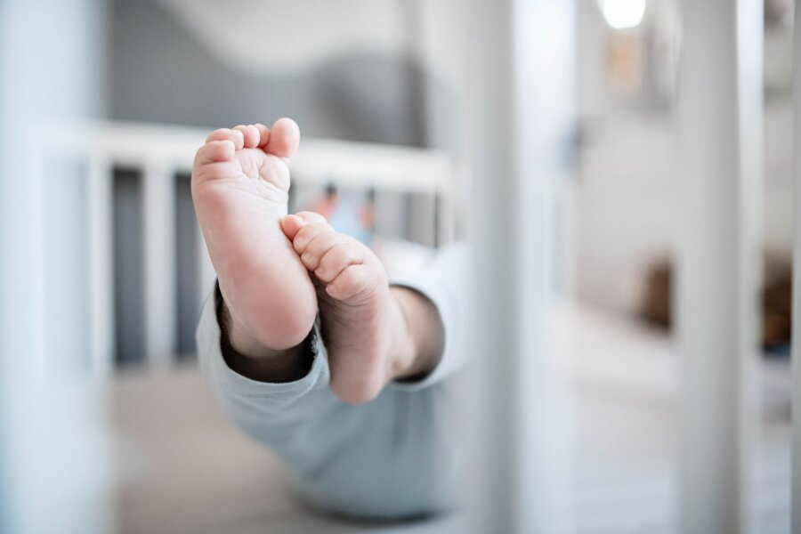 Hanna und Emil waren 2023 beliebteste Babynamen in Sachsen - Die Füße eines Babys sind in einem Kinderbett zu sehen.