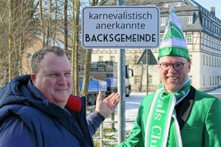 Hat Gelenaus Ortschef seine Wette erfüllt? - Gelenaus Bürgermeister Knut Schreiter zeigt Yannic Cyffka, dem Vorsitzenden des 1. Gelenauer Carnevalsclubs, das neue Schild am Orteingangsschild. 