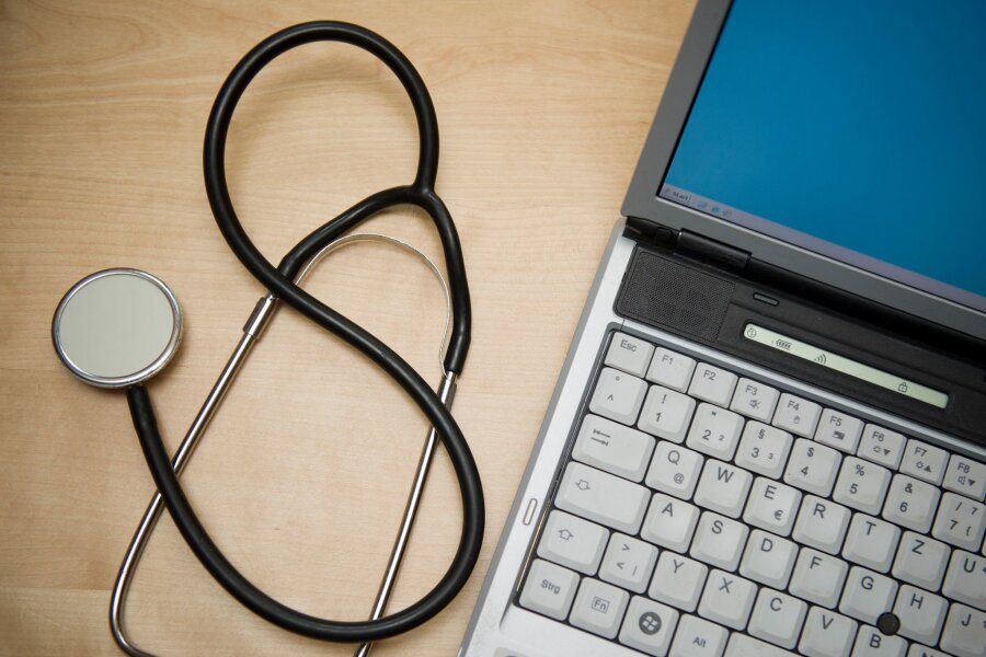 Hausärzte beklagen technische Probleme in Praxen - Ein Stethoskop liegt neben einem Laptop.