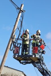 Havarie: Telefonmastgerät in Schieflage - Feuerwehrleute kappen die Leitung, damit der Telefonmast nicht auf die Straße stürzt. 