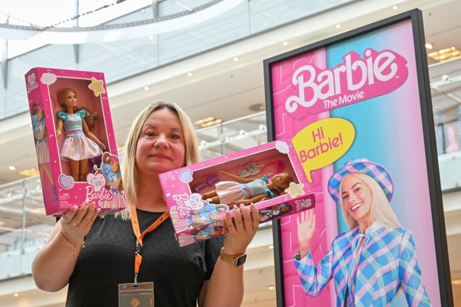 Hi Barbie, Hi Chemnitz! Ein Kinofilm schlägt pinke Wellen - Kaufhof-Mitarbeiterin Nicole Zahn präsentiert zwei Barbie-Puppen vor dem Aufsteller zum Kinofilm mit Schauspielerin Margot Robbie.