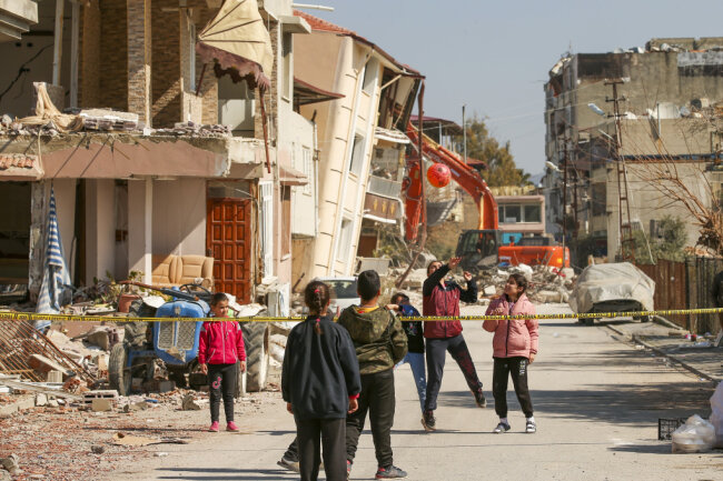 Samandag ( Türkei): Kinder spielen mit einem Ball neben zerstörten Gebäuden. Die Überlebenden des Erdbebens, das die Türkei und Syrien erschütterte und bei dem Zehntausende von Menschen ums Leben kamen und Hunderttausende obdachlos wurden, sind erneut Opfer eines weiteren tödliches Nachbebens geworden, welches die Region erschütterte.