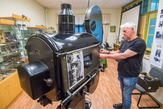 Joachim Siegert, ehemaliger Leiter des Auerbacher Kinos, beim Einrichten des alten Projektors der Einrichtung. Das historische Schwarz-Weiß-Foto im Vordergrund zeigt ihn bei derselben Tätigkeit in den 1970er-Jahren. 