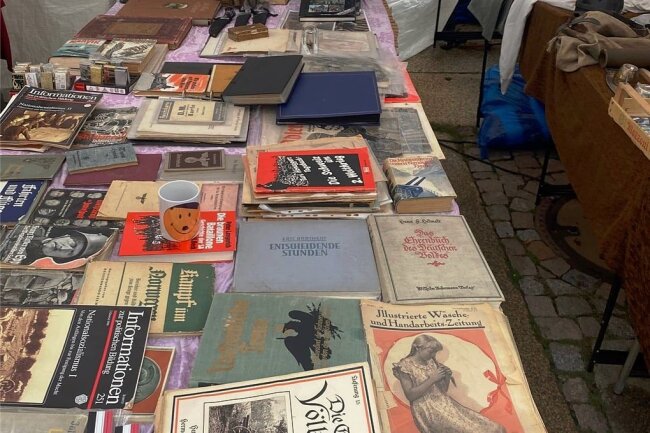 Hitlertasse und fragwürdige Schriften: Zwickauer Grünen-Stadtrat kritisiert Stadtfest-Buden - Feilgebotene Ware an einem Stand auf dem Stadtfest, dazu gehört auch eine Tasse mit stilisiertem Hitler-Gesicht. 