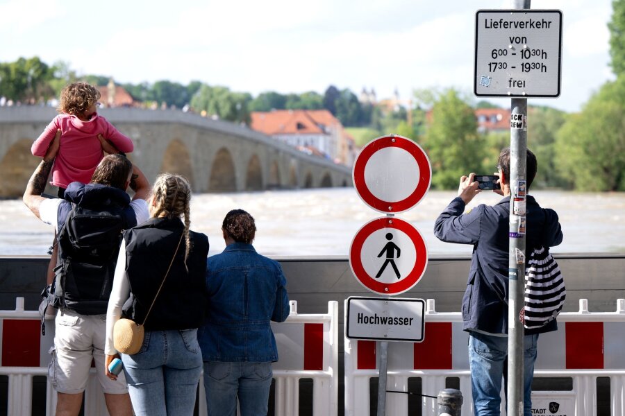 Hochwasserlage in Bayern entspannt sich - Menschen schauen sich in der Altstadt am Donauufer hinter einer Schutzwand das Hochwasser an.