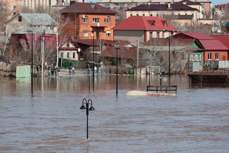 Hochwasserlage in Russland bleibt angespannt - Anwohner stehen an einer Absperrung und beobachten ein überschwemmtes Gebiet im russischen Orenburg.